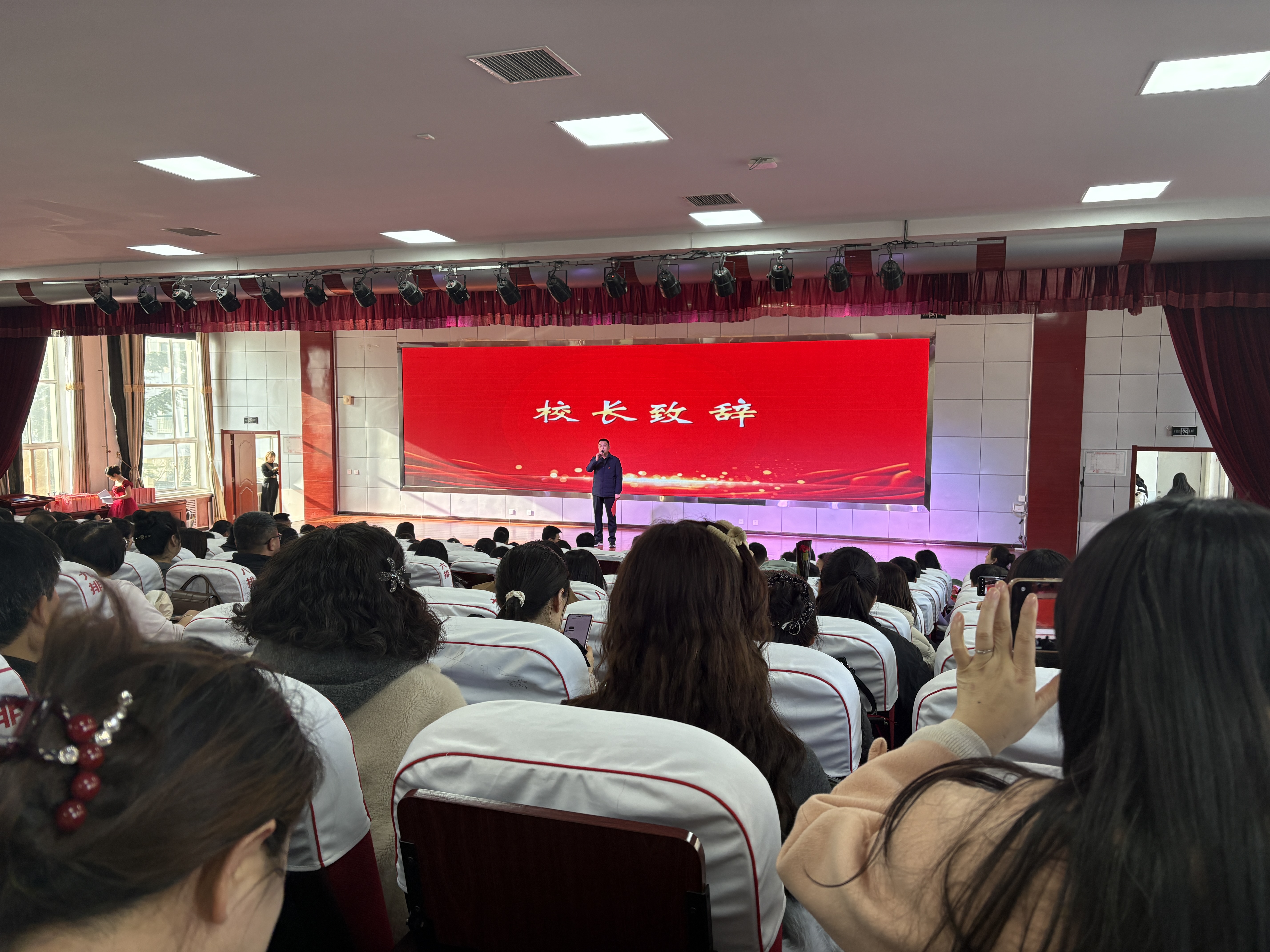 教师节庆祝活动，老师们身着正装，面带笑容，背景有鲜花装饰